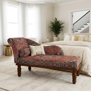 May include: A chaise lounge featuring a red, blue, and cream patterned fabric with a scrolled backrest and dark wooden legs. The piece includes a matching cylindrical bolster pillow and a rectangular cream-colored accent pillow with gold stripes.