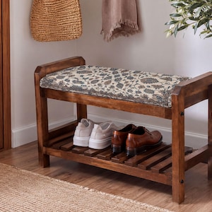 A wooden bench with a woven seat and storage space underneath, placed in a hallway with a woven basket and a potted plant nearby.