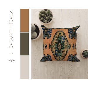 May include: A square throw pillow with a geometric pattern in shades of orange, blue, green, and black. The pillow is on a light wood surface.