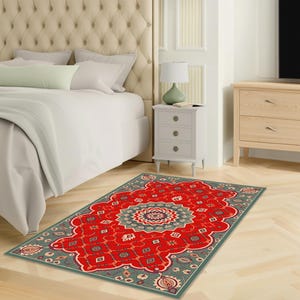 May include: A rectangular red rug with a central medallion design and a teal border. The rug features a detailed floral pattern in shades of teal, cream, and red. The rug is placed on a light-colored wooden floor in a bedroom setting.