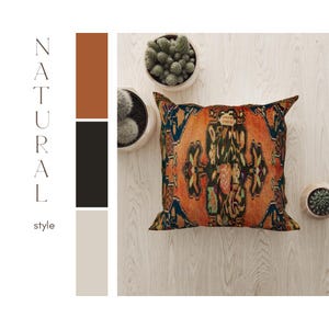 May include: A square cushion with a colourful, intricate pattern in shades of orange, red, green, blue, and black. The cushion is on a light wood surface with a few small green plants in pots.