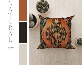 Puede incluir: Una almohada cuadrada con un patrón colorido e intrincado en tonos de naranja, rojo, verde, azul y negro. La almohada está sobre una superficie de madera clara con algunas pequeñas plantas verdes en macetas.