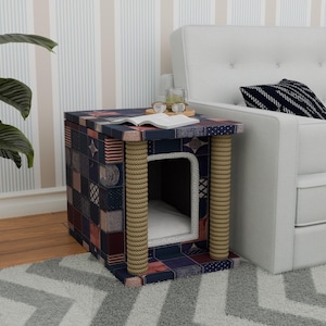 May include: A blue and red patterned cat bed with a rope-wrapped entrance. The bed is on a small table with a white couch in the background.