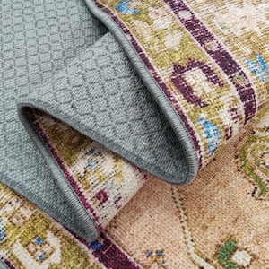 K&ouml;nnte beinhalten: Nahaufnahme eines Teppichs mit einem Muster in Braun-, Beige-, Gr&uuml;n- und Lilat&ouml;nen. Der Teppich hat eine graue R&uuml;ckseite mit einem Rautenmuster.