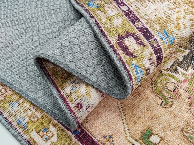 K&ouml;nnte beinhalten: Nahaufnahme eines Teppichs mit einem Muster in Braun-, Beige-, Gr&uuml;n- und Lilat&ouml;nen. Der Teppich hat eine graue R&uuml;ckseite mit einem Rautenmuster.