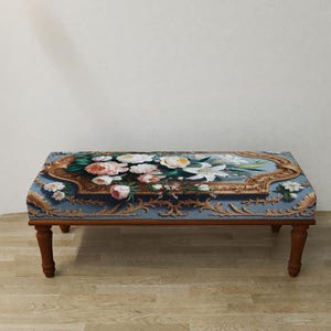 May include: A rectangular ottoman with a floral tapestry top featuring pink, white, and yellow flowers on a blue background. The wooden frame has four brown legs.