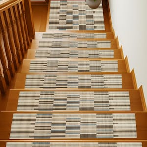 May include: Wooden staircase with patterned stair treads. The treads feature a geometric design in shades of beige, gray, and blue. A matching rug is at the top of the stairs, and a potted plant sits nearby. The wooden handrail and steps have a warm, natural finish.