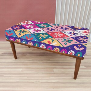 Peut inclure: Un ottoman coloré à motifs avec une structure en bois. L'ottoman présente un motif géométrique avec des couleurs rose, bleu, vert, jaune et rouge.