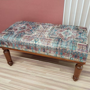 Puede incluir: Un banco de madera con un coj&iacute;n de tela estampado. El coj&iacute;n presenta un dise&ntilde;o geom&eacute;trico colorido en tonos azules, rojos y beige.