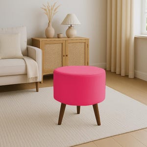 May include: A round, hot pink ottoman with dark brown wooden legs. The upholstered seat is a vibrant solid color. The legs are angled and evenly spaced, providing a stable base. This accent furniture piece is suitable for a living room or bedroom.