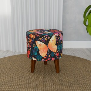 May include: A round, floral patterned ottoman with wooden legs. The ottoman features a large butterfly design with orange wings and a black body.