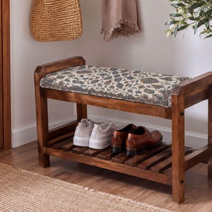 A wooden bench with a woven seat and storage space underneath, placed in a hallway with a woven basket and a potted plant nearby.