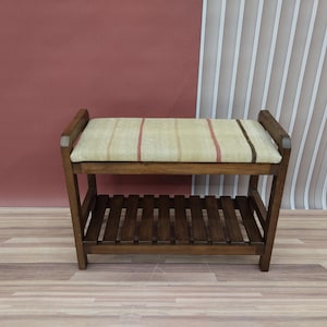 May include: A wooden bench with a lower shelf. The seat cushion is beige with red and brown stripes. The frame is a dark brown colour. The bench is a piece of furniture.