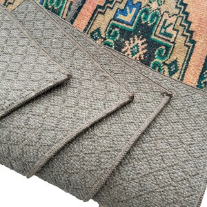 Puede incluir: Primer plano de una pila de cuatro alfombras grises con textura tejida. Las alfombras est&aacute;n dobladas una encima de la otra, mostrando los bordes y el patr&oacute;n tejido.