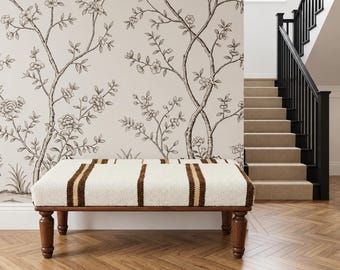 May include: A rectangular ottoman featuring a cream-coloured woven fabric top with vertical dark brown stripes. The base is constructed from dark wood and supported by four turned legs. The piece is positioned in front of a wall with floral wallpaper.