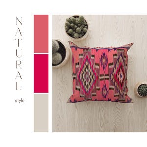 Puede incluir: Una almohada de tiro rosa y roja con un patrón geométrico. La almohada está sobre una superficie de madera clara con dos pequeñas plantas en maceta.