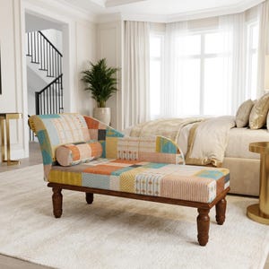May include: A chaise lounge featuring a patchwork fabric upholstery in shades of orange, blue, yellow, and white with various geometric patterns. The furniture piece has a curved backrest, a cylindrical bolster pillow, and four dark brown wooden legs.
