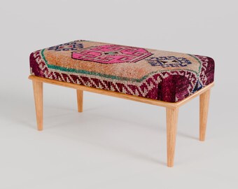 May include: A wooden bench with a colourful patterned cushion. The cushion has a pink, red, blue and green geometric design.
