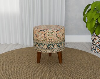 May include: A round, patterned ottoman with a floral design in shades of pink, blue, and green. The ottoman has four wooden legs and is sitting on a brown rug.