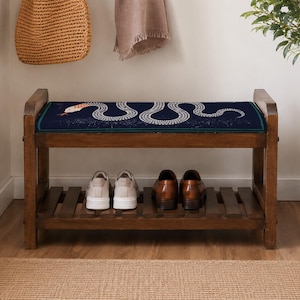 A wooden bench with a blue and white snake design on the seat, displaying a pair of shoes on the lower shelf.