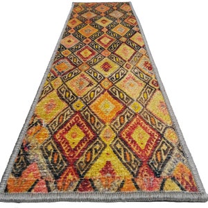 May include: A long, narrow runner rug with a geometric pattern in shades of orange, yellow, red, and black. The rug has a gray fringe border.