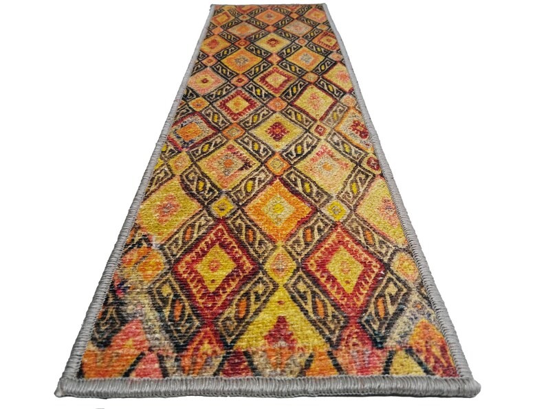 May include: A long, narrow runner rug with a geometric pattern in shades of orange, yellow, red, and black. The rug has a gray fringe border.