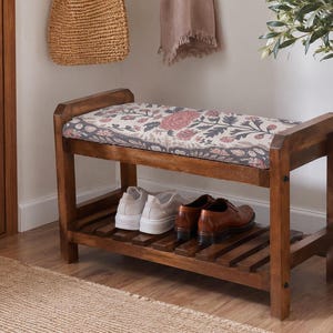 A wooden bench with a floral patterned seat and storage space underneath, situated in a hallway with a woven basket and a potted plant nearby.