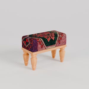 May include: A small wooden stool with four legs and a colorful patterned fabric seat. The fabric has a geometric design with shades of red, green, and purple.
