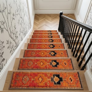 Puede incluir: Un juego de alfombrillas rectangulares para escaleras con una base de color naranja y rojo vibrante con patrones geométricos repetitivos en negro y dorado. Cada alfombrilla tiene un borde gris oscuro, instalada en escaleras de madera con barandilla negra.