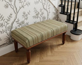 May include: A rectangular bench featuring a cushioned seat upholstered in a textured olive green fabric with vertical brown and tan stripes. The bench is supported by four turned wooden legs with a dark brown finish and a smooth, polished surface.