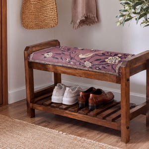 May include: A wooden entryway bench with a dark brown finish and a rectangular seat cushion upholstered in a mauve fabric featuring a cream-coloured floral and bird pattern. The bench includes a slatted lower shelf for shoe storage.