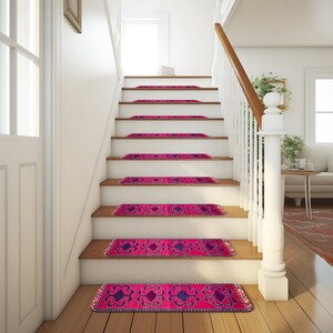 May include: A set of pink and purple patterned stair treads with a fringed border. The treads are placed on a wooden staircase with a white railing.