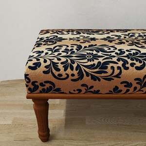 Puede incluir: Un otom&aacute;n decorativo con un estampado floral beige y azul marino. El marco y las patas de madera son de color marr&oacute;n c&aacute;lido. El otom&aacute;n es un mueble elegante.
