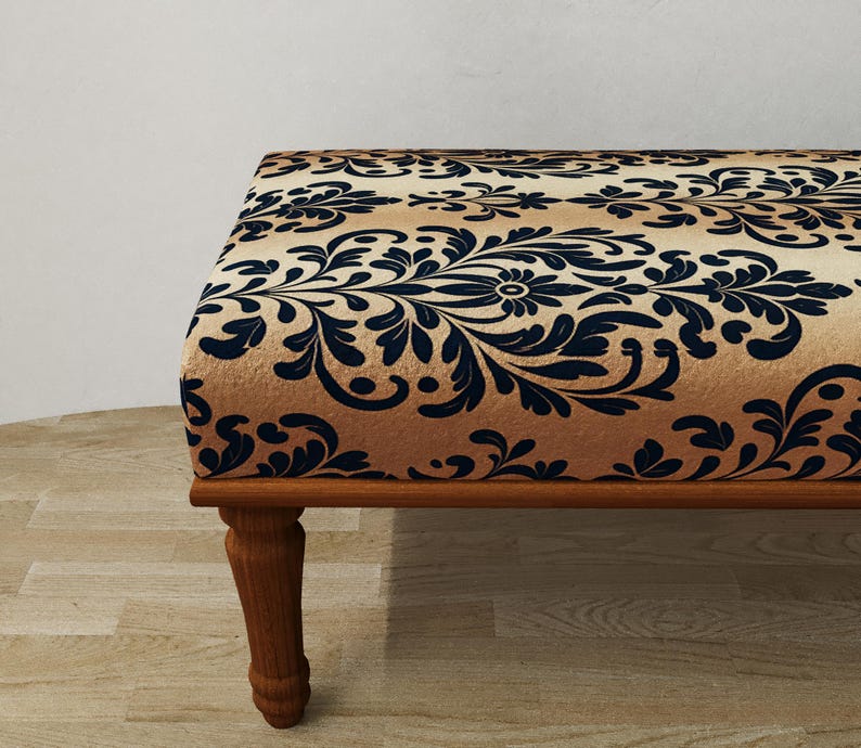 Puede incluir: Un otom&aacute;n decorativo con un estampado floral beige y azul marino. El marco y las patas de madera son de color marr&oacute;n c&aacute;lido. El otom&aacute;n es un mueble elegante.