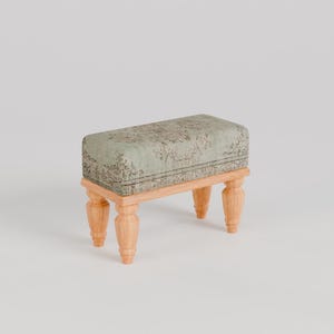 Könnte beinhalten: Ein kleiner, rechteckiger Hocker mit einer hellgrünen, gemusterten Stoffoberfläche und vier Holzbeinen.