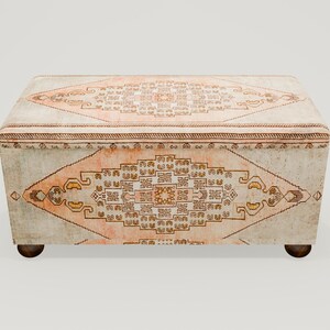 May include: A white and beige storage ottoman with a traditional patterned rug design. The ottoman has rounded legs and a rectangular shape.