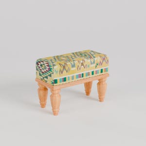 May include: A small wooden stool with four legs and a yellow, green, and red patterned cushion.