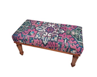 May include: A wooden bench with a pink, blue and green patterned cushion. The cushion has a traditional rug design.