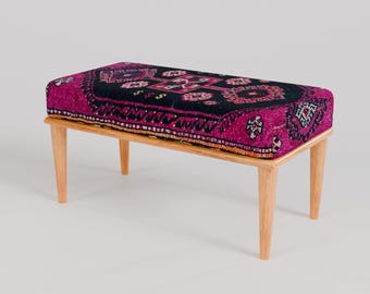 May include: A wooden bench with a pink and black patterned cushion. The cushion has a traditional Turkish rug design.