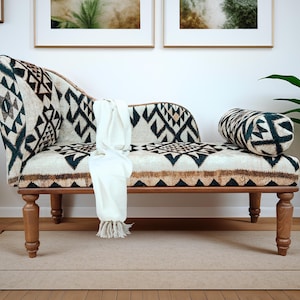 Può includere: Una chaise longue con motivo bianco e nero con gambe in legno. Una coperta bianca è drappeggiata sulla chaise longue. La chaise longue è su un tappeto beige.