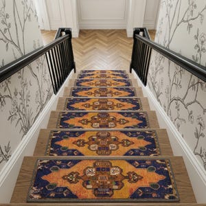 May include: A set of rectangular stair treads featuring a vibrant orange and deep blue geometric pattern. Each tread is centered on a wooden step between black railings, with white walls decorated with black and white floral wallpaper.