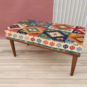 Puede incluir: Un otomano con estampado colorido y marco de madera. El otomano tiene un diseño geométrico con colores rojo, azul, verde y amarillo.