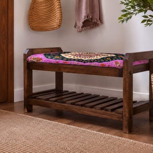 a wooden bench with a colorful, patterned seat, placed in a room with a woven basket and a potted plant.