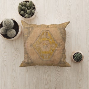 May include: A beige throw pillow with a yellow and gray geometric pattern. The pillow is on a light wood surface with two potted succulents.