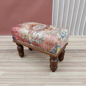 May include: A small wooden footstool with four turned legs. The top is upholstered in a colourful patterned fabric with shades of red, blue, and yellow.