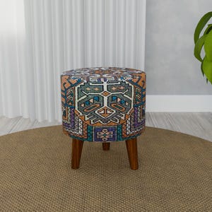 Può includere: Un pouf rotondo e colorato con un motivo geometrico in tonalità di blu, arancione, verde e viola. Il pouf ha quattro gambe in legno.