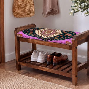 A wooden bench with a colorful patterned seat and a pair of shoes placed on it, situated in a hallway with a woven basket and a potted plant nearby.