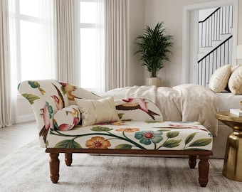 May include: A chaise lounge featuring a cream-colored fabric upholstery with a colorful pattern of birds, green leaves, and orange and blue flowers. The furniture piece has dark wooden legs and includes a small cylindrical bolster and a rectangular pillow.