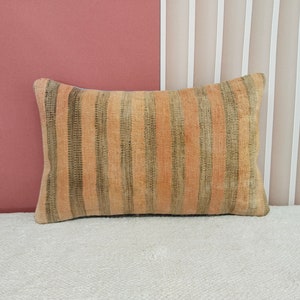 Puede incluir: Una almohada rectangular con rayas beige y verdes. La almohada está hecha de una tela suave y texturizada.