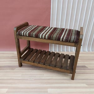 May include: A wooden bench with a brown and white striped cushion. The bench has a lower shelf for storage.